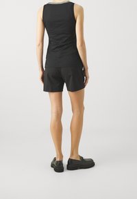 Svart ärmlös topp med vitrandig halsringning, ihop med svarta shorts. Modellen står med svarta skor på en neutral bakgrund.