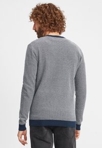 Grå texturerad tröja med hexagonmönster, marinblå ribbad krage och muddar, långa ärmar och en vanlig passform.