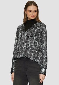 Blouse en imprimé serpent noir et blanc avec un décolleté en V, des manches longues et une coupe décontractée. Elle présente un tissu lisse et un ourlet légèrement courbé.