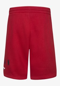 Pantalones cortos deportivos rojos hechos de tela suave, con un diseño de color sólido y logotipo negro en la pierna izquierda. Cintura elástica para mayor comodidad.