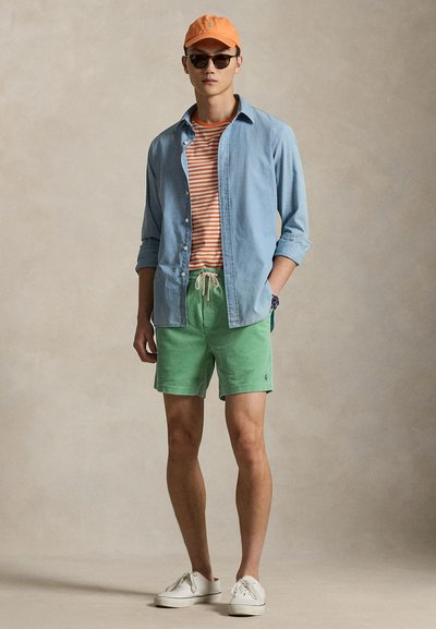 Ανοιχτό μπλε πουκάμισο με κουμπιά πάνω από πορτοκαλί ριγωτό μπλουζάκι; πράσινα σορτς με κορδόνι; πορτοκαλί καπέλο; μαύρα γυαλιά ηλίου; λευκά παπούτσια.