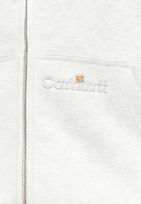 Φούτερ με κουκούλα σε ανοιχτό γκρι χρώμα, με μεταλλικό φερμουάρ και λευκό λογότυπο Carhartt κεντημένο κοντά στην τσέπη.