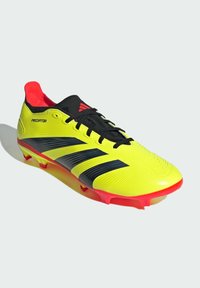 Scarpini da calcio gialli con strisce e dettagli neri, upper testurizzato, interno rosso e suola rossa. Presentano un design con lacci e una forma aerodinamica.