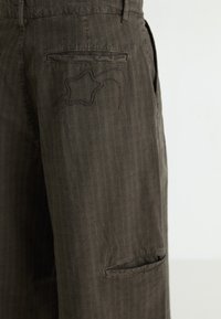 Pantalons brown à rayures fines avec une poche arrière ornée de broderies décoratives et une poche latérale, fabriqués en tissu doux.
