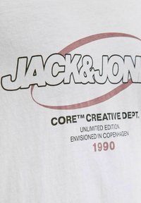 Jack & Jones logo uz balta auduma ar tekstu "CORE™ CREATĪVAIS DEPARTAMENTS. Neierobežotā izdevumā. Izdomāts Kopenhāgenā 1990."