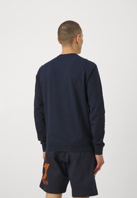 Felpa blu navy vista da dietro, con collo rotondo e maniche lunghe. Il materiale sembra morbido, con una texture liscia e polsini a coste.