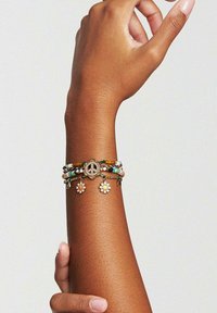 Bracelet multicolore en perles avec un charm en forme de symbole de paix et des accents floraux, fabriqué à partir de matériaux mélangés avec une texture lisse.