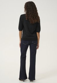 Suéter negro de manga corta con un corte relajado, hecho de un material brillante. Se combina con unos jeans oscuros de campana que cuentan con un diseño de cinco bolsillos.