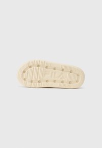 Cream-colored sneaker sole featuring prominent grooves, dots for traction, and Fila logo embossed in the center. Smooth rubber texture.