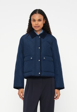 Navy quilted jacket with a collared neck, snap buttons, and two front pockets. Features ribbed hem and cuffs for added texture.