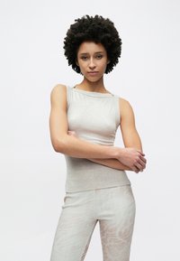 Top grigio chiaro senza maniche con scollo dritto e design aderente, abbinato a pantaloni chiari con motivo in un tessuto morbido e strutturato.