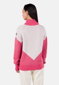 Sweter dzianinowy z wysokim różowym prążkowanym kołnierzem, w kolorach różowym jasnym i intensywnym różowym, z v-kształtnym wzorem na plecach.