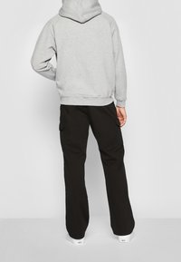 Sudadera gris con capucha y bolsillo tipo canguro, combinada con pantalones cargo negros con bolsillos laterales y un corte holgado, completada con zapatillas blancas.