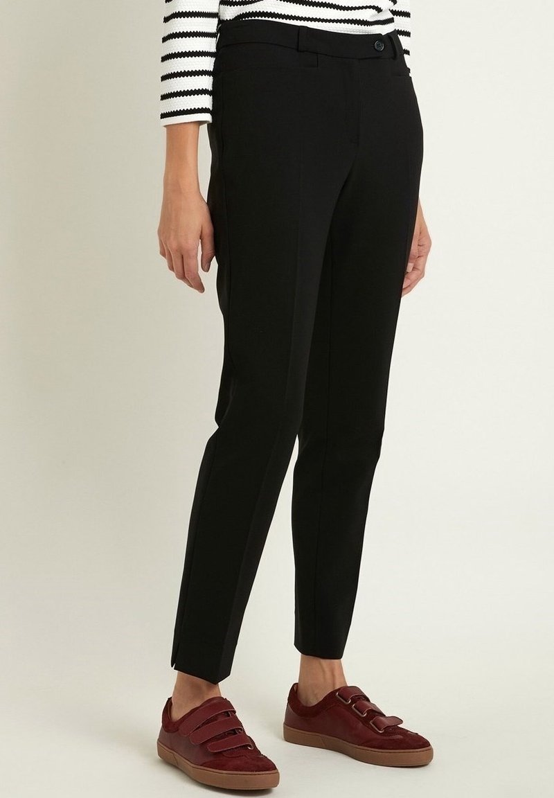 Černé formální kalhoty s přiléhavým střihem, s plochým předním dílem, postranními kapsami a minimalistickým designem. Nosit s vínovými teniskami.