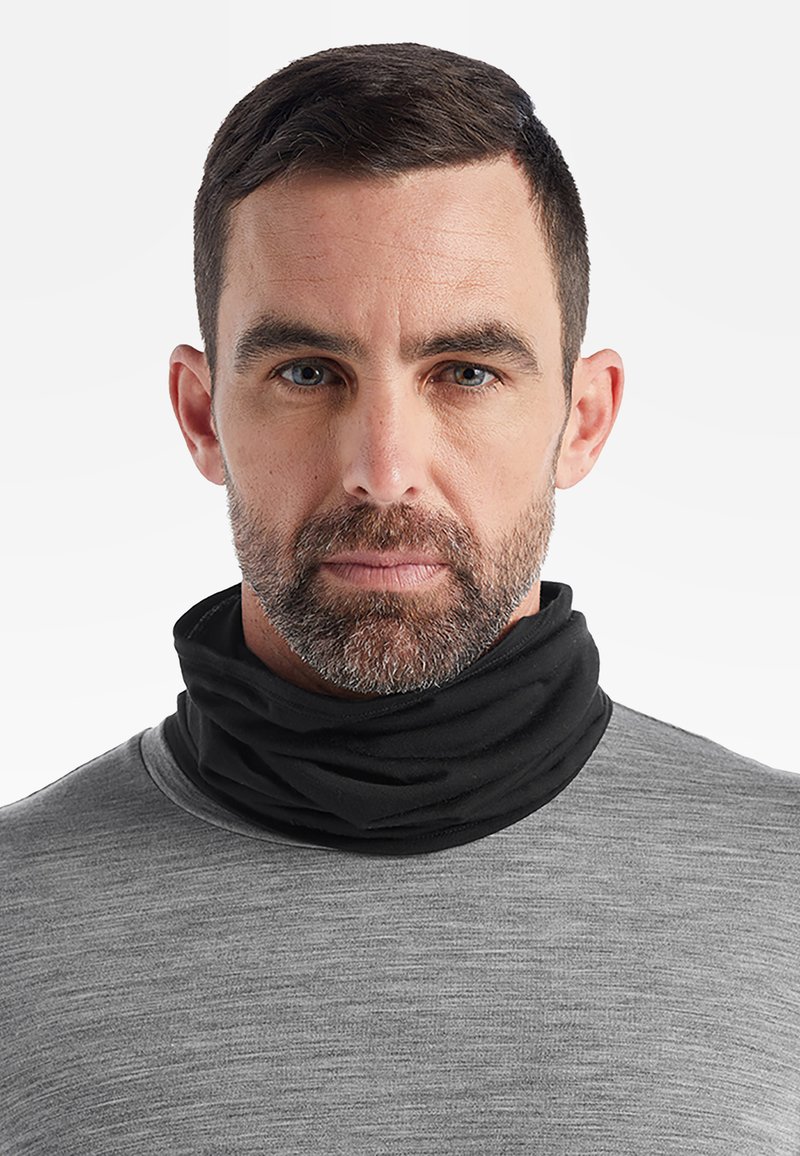 Svart halsduk av mjukt, elastiskt tyg, som bärs över en grå långärmad tröja, med en enkel och sömlös design.