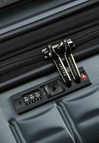 Valise noire texturée avec des accents métalliques, dotée de doubles zips, d'un verrou à combinaison approuvé par la TSA et d'un indicateur de système de sécurité.