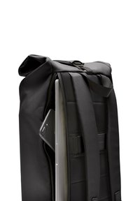 Sac à dos noir avec des bretelles réglables, fabriqué en tissu texturé. Ordinateur portable partiellement visible, avec un téléphone dans une poche latérale. Fermeture éclair.