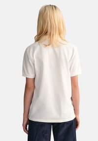T-shirt en coton blanc avec une coupe décontractée et des manches courtes, affichant une encolure ronde et une texture lisse. Assorti à un pantalon en velours côtelé bleu marine.
