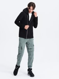 Zwarte zip-up hoodie met een capuchon, gedragen over een wit T-shirt. Gecombineerd met lichtgroene cargo-broeken met meerdere zakken. Zwarte sneakers.