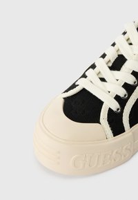 Sapatilha em tela preta com detalhes em creme, sola de borracha e texturas. Apresenta atacadores brancos e um logótipo no calcanhar.