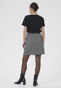 T-shirt noir à manches courtes associé à une jupe grise à rayures noires, longueur genoux, complété par des collants noirs transparents et des bottines noires à talons.