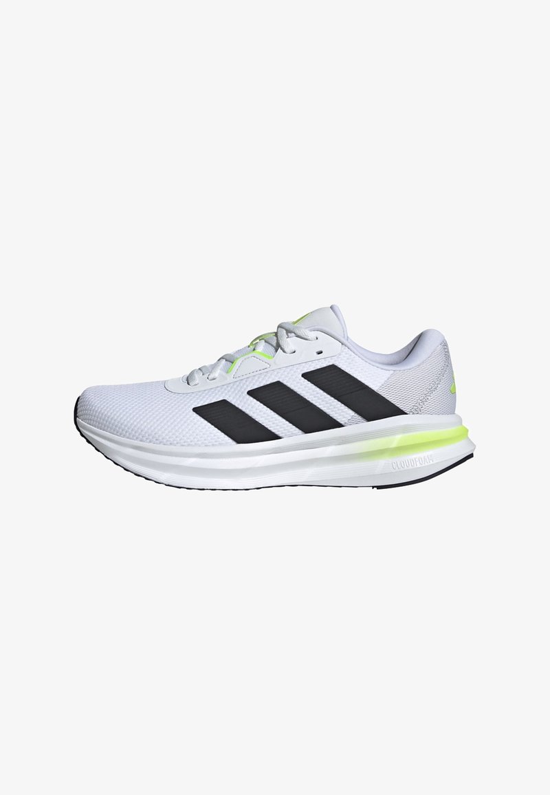 Zapatilla deportiva blanca con rayas negras y acentos verdes, con un upper de malla texturizada, diseño de cordones y suela acolchada para mayor soporte.