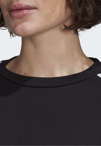 Svart bomullströja med rund hals, slät struktur och en vit detalj längs axelsömmen. Närbild av halsringningen och nacken.