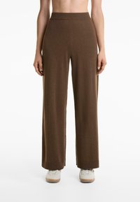 Pantaloni marroni a gamba larga realizzati in un tessuto morbido e testurizzato, con una vita alta e una lunghezza lunga; abbinati a scarpe color tan.