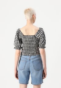 Black and white checkered puff-sleeve top with a smocked back, paired with high-waisted blue denim shorts. Smooth texture, casual fit.