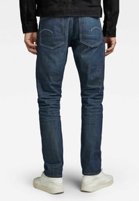 Dopasowane dżinsy o wąskim kroju w ciemnym niebieskim kolorze, z klasycznym pięciokieszeniowym designem i subtelnymi przeszyciami na tylnych kieszeniach.