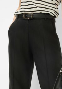 Black trousers made from a smooth, lightweight fabric. Features a classic fit, side pockets, and a slim black belt with a gold buckle detail.