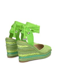 Sandales compensées vertes avec des brides en tissu texturé, tige en daim et un design en jute tressé superposé. Comprend des accents métalliques et des liens en ruban.