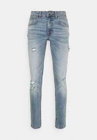 Jeans de mezclilla azul claro con corte ajustado, que presentan detalles desgastados y múltiples rotos. Diseño clásico de cinco bolsillos con cierre de botón metálico.