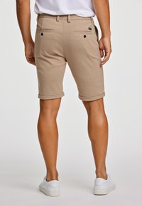 Beżowe szorty z miękkiego materiału, z podwiniętymi mankietami, dwoma tylnymi kieszeniami z czarnymi guzikami oraz teksturowanym wykończeniem.