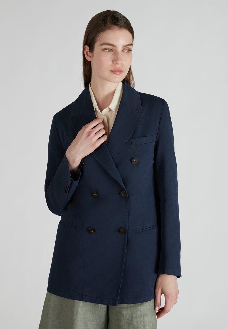 Blazer doppiopetto blu navy in tessuto leggero con colletto a rever, due tasche frontali e bottoni scuri, abbinato a una camicetta chiara.