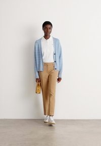 Light blue knitted cardigan, white polo shirt, beige trousers, white sneakers, holding a small yellow handbag. Simple, casual outfit design.