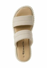 Beige glid sandaler med två breda, platta remmar, en texturerad fotbädd och en vit skulpterad sula. Har logotypen på insidan.