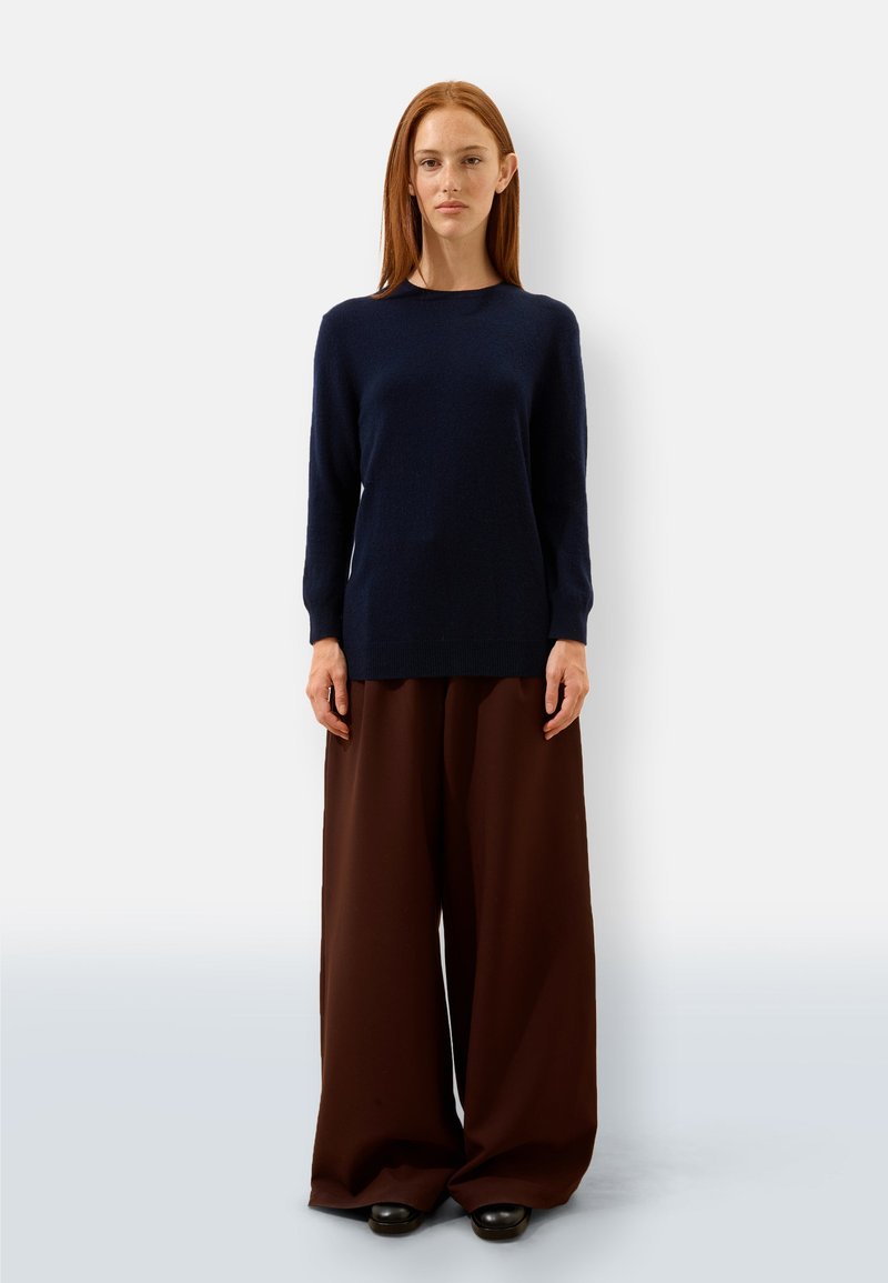 Granatowy sweter z dzianiny z długimi rękawami i okrągłym dekoltem, połączony z luźnymi, ciemnobrązowymi spodniami typu wide-leg i czarnymi butami.