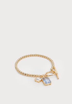 Pulseira de contas em tom de ouro, com duas pedras retangulares, uma transparente e outra azul clara, apresentando um fecho de toggle e um detalhe em elos circulares.