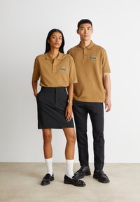 Ruske lyhythihaiset kauluspaidat, joissa on brodeerattu vihreä logo, yhdistettynä mustaan kynähameeseen ja mustiin housuihin, molemmat sileästä kankaasta.