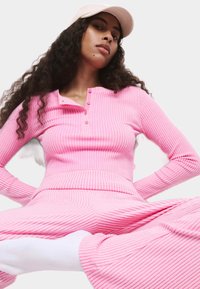 Roze geribbelde lange mouw top met een henley kraag en drie knopen, gecombineerd met bijpassende broek. Witte sokken, zachte textuur.