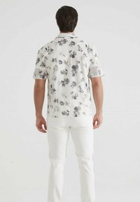 Chemise à manches courtes à fleurs blanches avec motifs gris ; coupe décontractée ; texture lisse ; associée à un pantalon blanc.