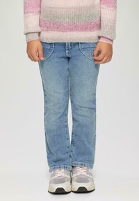 Jasnoniebieskie dżinsy o prostym kroju, z widocznymi przednimi kieszeniami i wypłowiałym wykończeniem. W połączeniu z masywnymi, szaro-białymi trampkami.