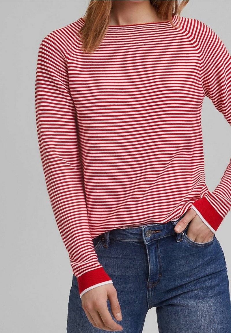 Femme portant un haut à manches longues rayé horizontalement rouge et blanc, rentré dans un jean en denim bleu, avec une main dans la poche.