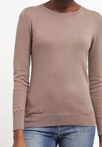 Ljust rosa långärmad tröja med ribbad rundhalsning och åtsittande ärmmuddar, tillverkad av mjukt material, i kombination med denimjeans.