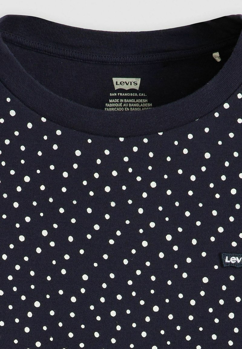 Camiseta azul marino con lunares blancos, cuello redondo acanalado y un pequeño parche negro con el logo de Levi's cerca de la parte inferior. Material de algodón.