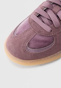 Μοβ αθλητικό παπούτσι με συνδυασμό σουέντ και λείων υλικών, στρογγυλεμένη μύτη, υφή επιφάνειας και λαστιχένια σόλα με ελαφρώς διαφανές άκρο.