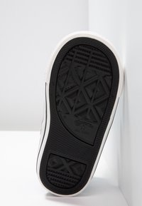 Czarna gumowa podeszwa z teksturowanymi wzorami grip. Białe wykończenie widoczne wzdłuż boków, z wytłoczonym logo "Converse All Star."