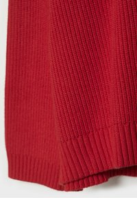 Tissu rouge tricoté avec une texture côtelée, présentant des plis et des motifs de tricot détaillés.