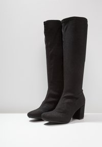 Botas negras hasta la rodilla, hechas de un tejido texturizado con un suave brillo, que presentan un tacón ancho y una punta redondeada.